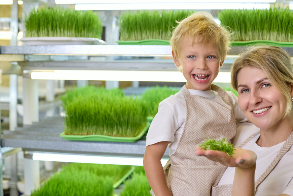 Pretty woman in her arms with a boy holds fresh micro-green shoots on her palm