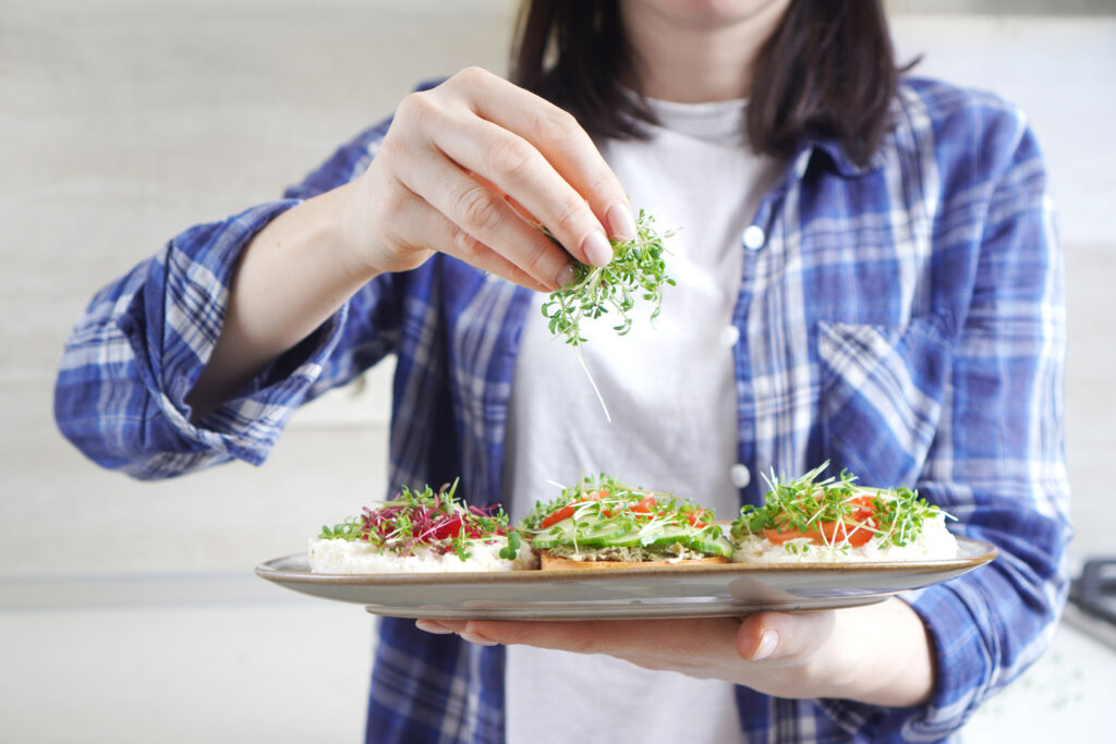 Woman doing healthy vegan toasts with microgreens on a breakfast.